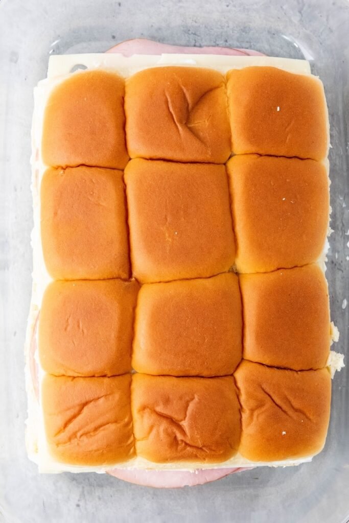 Overhead view of assembled bread with the top buns placed on, arranged tightly together in a baking dish before glazing and baking.