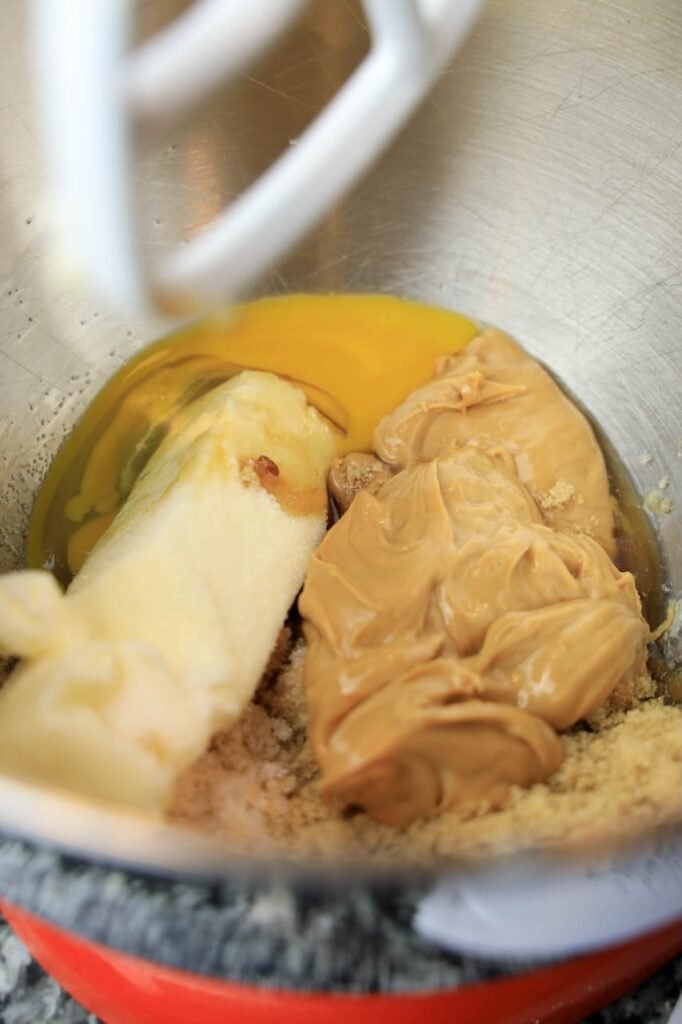 Peanut butter, softened butter, brown sugar, and an egg being mixed together in a stand mixer bowl to form the base of the cookie dough for Valentine’s M&M cookies.