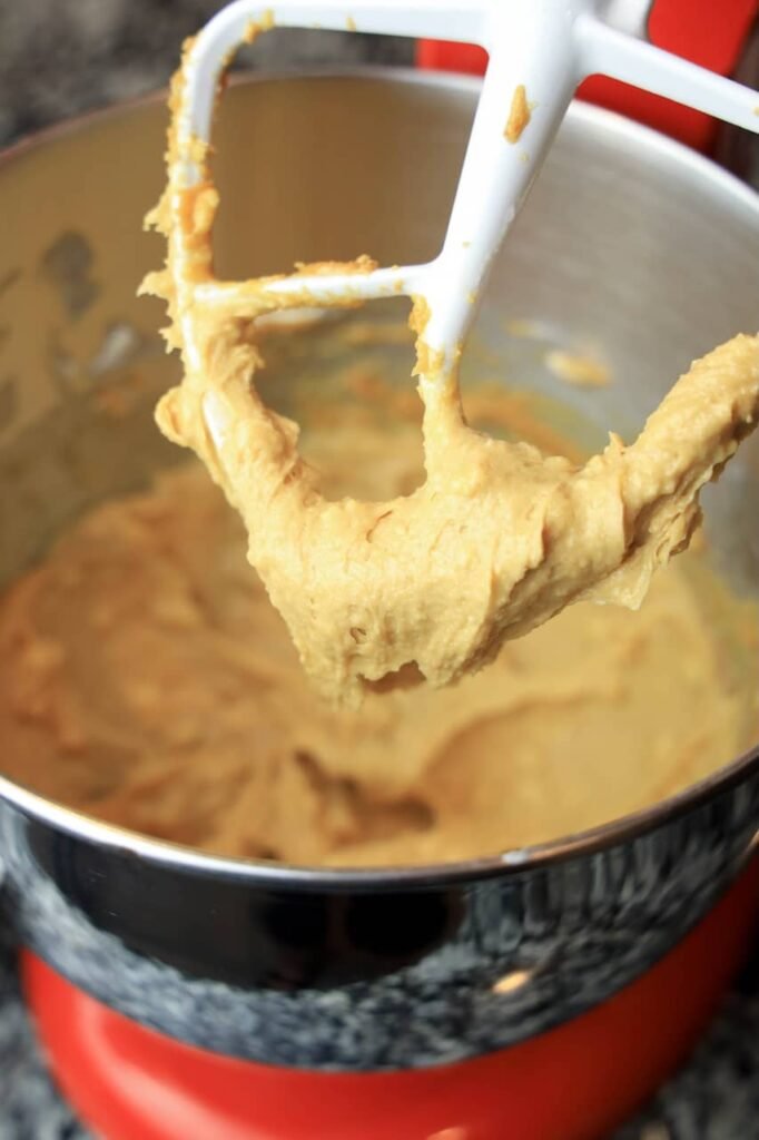 Thick peanut butter cookie dough clinging to a stand mixer paddle, showing the smooth, creamy consistency of the dough before Valentine’s M&M candies are mixed in.