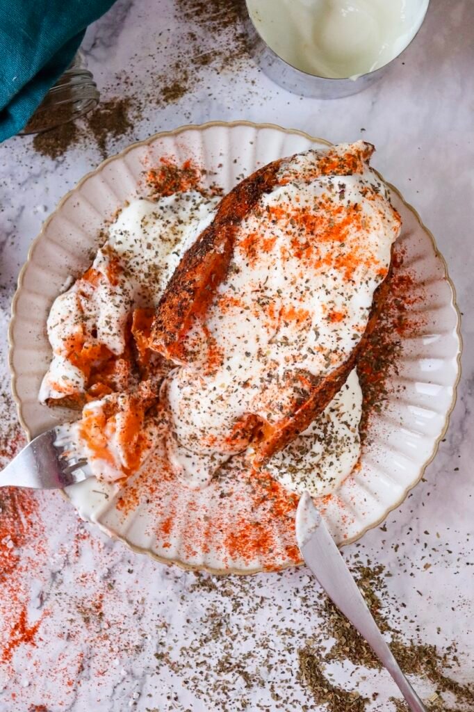 Close up of air fryer sweet potato jacket topped with Greek yogurt, paprika, and dried basil, partially cut open on a plate.