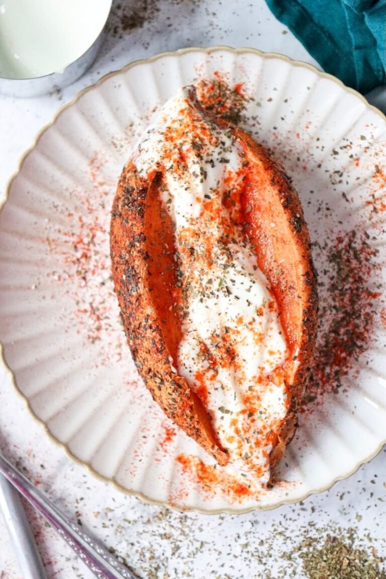 Air fryer sweet potato jacket split open and topped with Greek yogurt, paprika, and dried basil on a white plate.