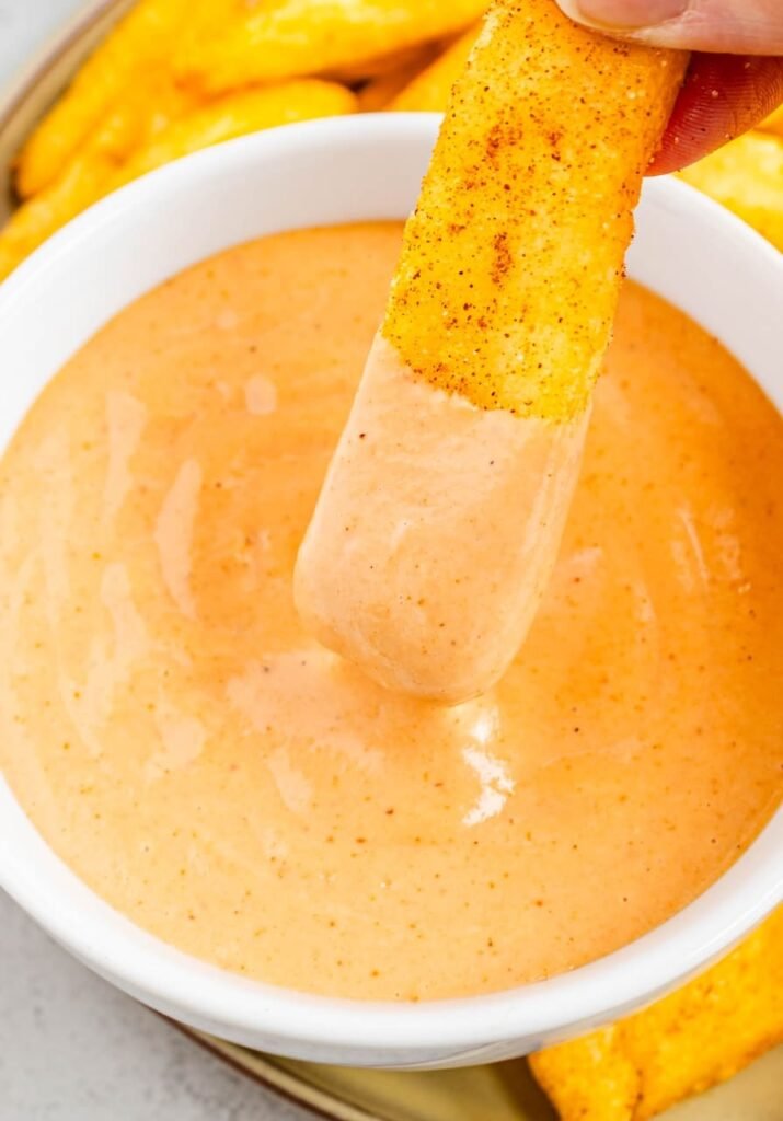 A seasoned fry being dipped into a bowl of creamy campfire sauce, showing the thick texture of an easy Red Robin–style copycat dipping sauce.