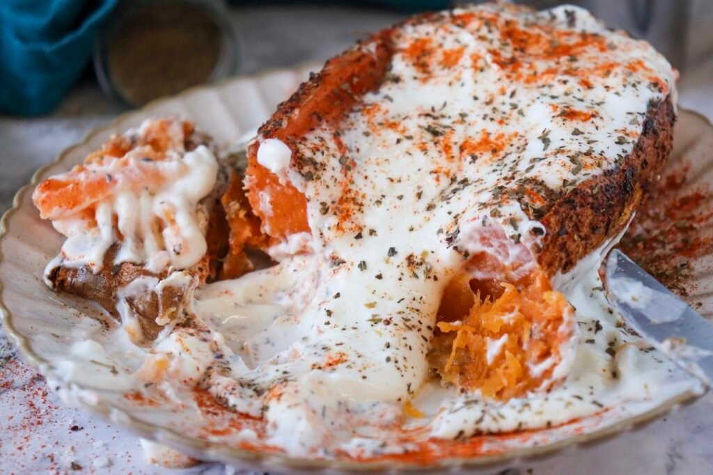 Close up of air fryer sweet potato jacket topped with Greek yogurt and herbs, partially sliced open with creamy sauce spread across the plate.