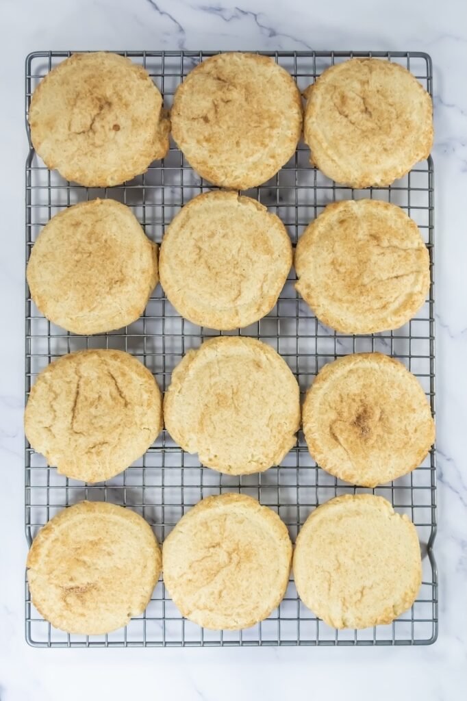 Overhead view of freshly baked desserts cooling on a metal wire rack, showing golden edges and soft centers before adding cinnamon buttercream frosting.