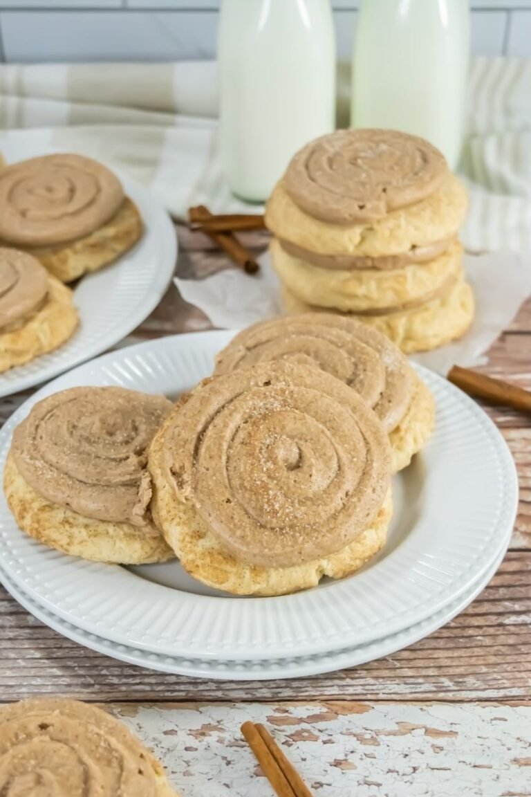 Stacked Crumbl churro cookies on white plates with cinnamon buttercream swirls and a light dusting of cinnamon sugar, styled with milk bottles and cinnamon sticks in the background.