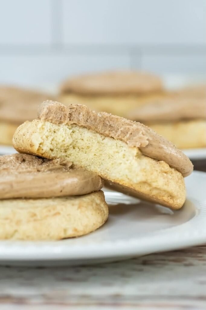 Close-up of a Crumbl churro cookie cut in half, showing the soft interior texture and topped with cinnamon buttercream frosting on a white plate.