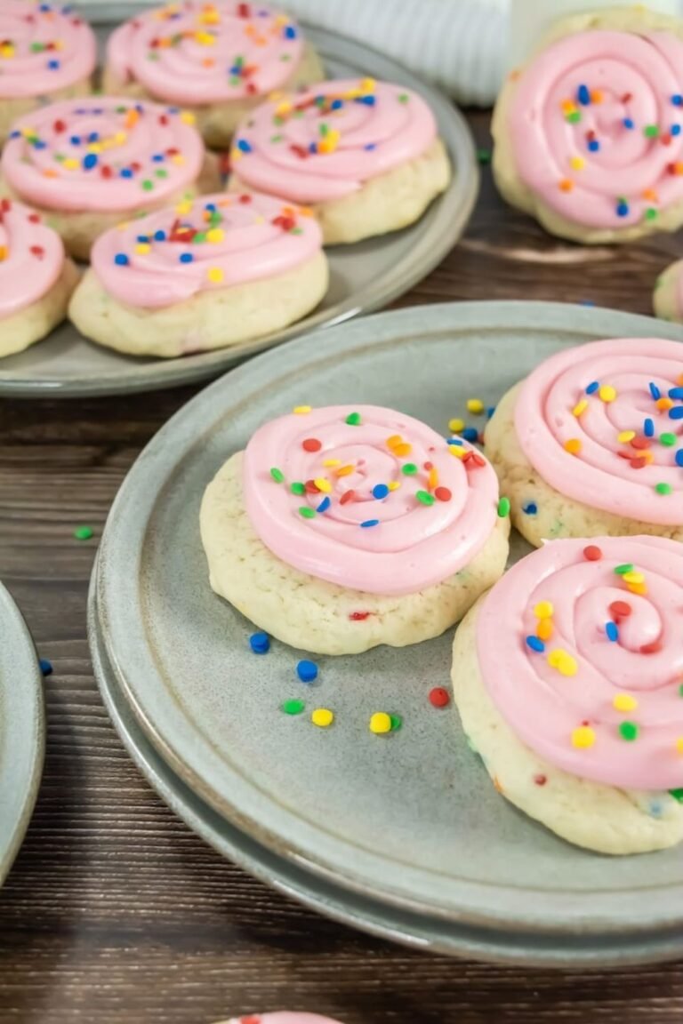 Confetti cake cookies topped with pink cream cheese frosting and colorful sprinkles, arranged on ceramic plates on a wooden table, showing the finished cookies ready to serve.