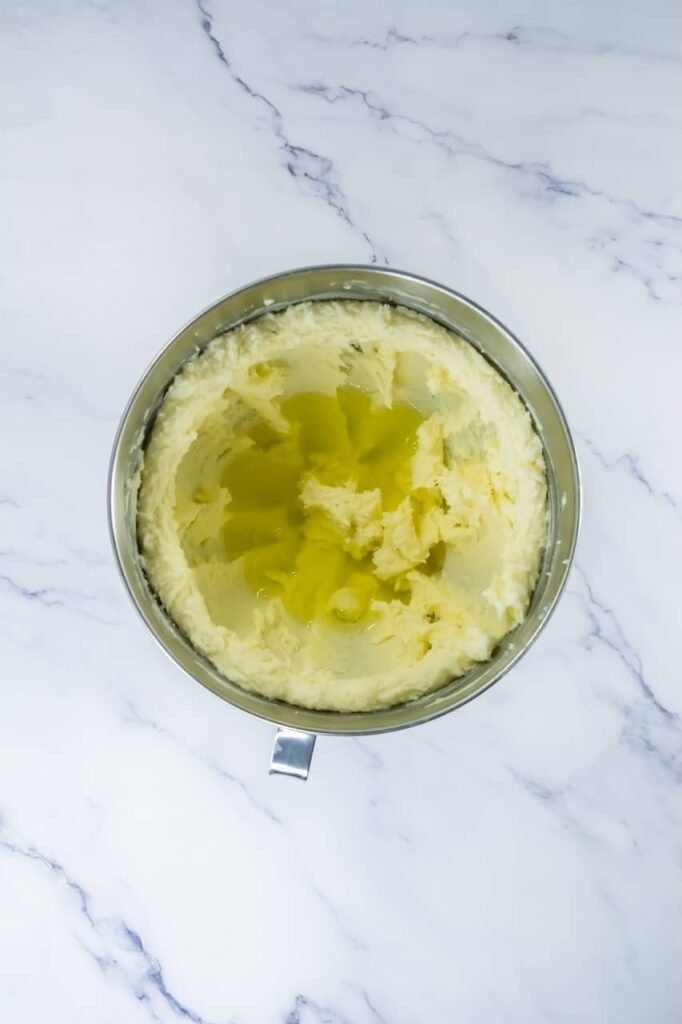 Overhead view of a stand mixer bowl filled with creamed butter and sugar, whipped until pale, light, and fluffy, with soft peaks and a smooth texture. This image shows the cookie dough base at the creaming stage, just before the egg whites, vanilla, and cake flavoring are added for making soft confetti cake cookies.