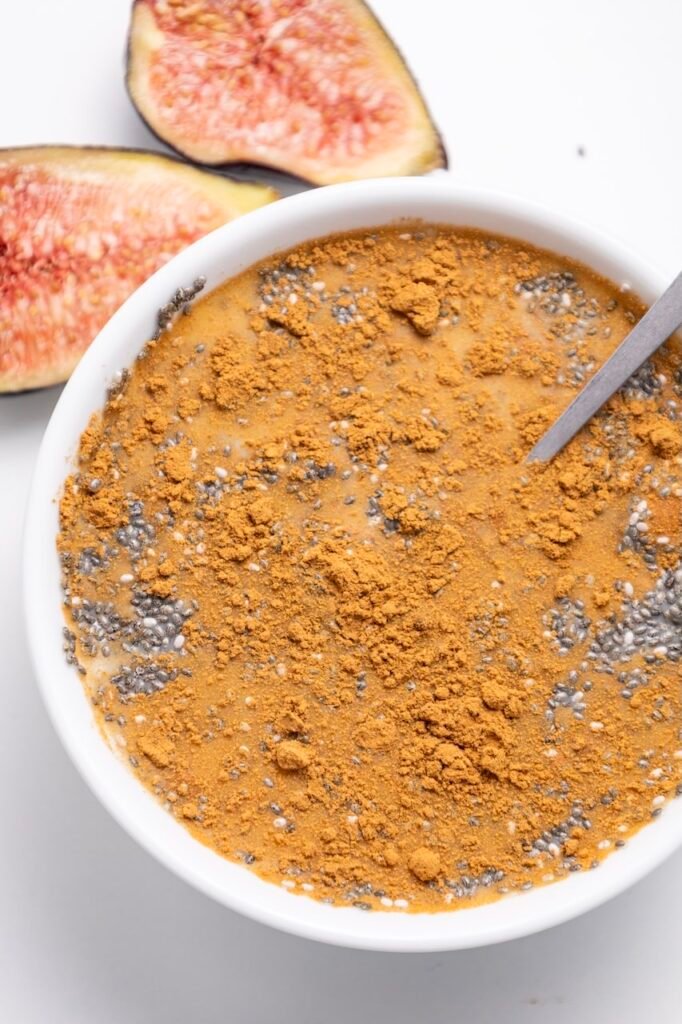 Close-up of creamy topped with cinnamon and seeds in a white bowl, with fresh halves in the background.