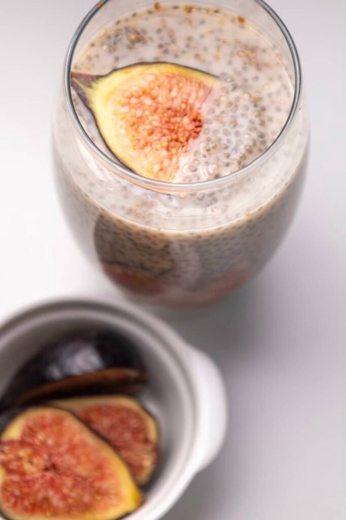 Glass jar filled with creamy made with oat milk, layered with fresh slices and set on a white background.