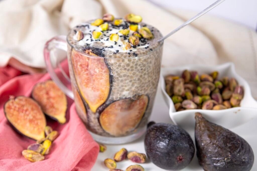 Glass mug filled with creamy chia mixture layered with fresh fig slices and topped with yogurt, pistachios, and black sesame seeds.