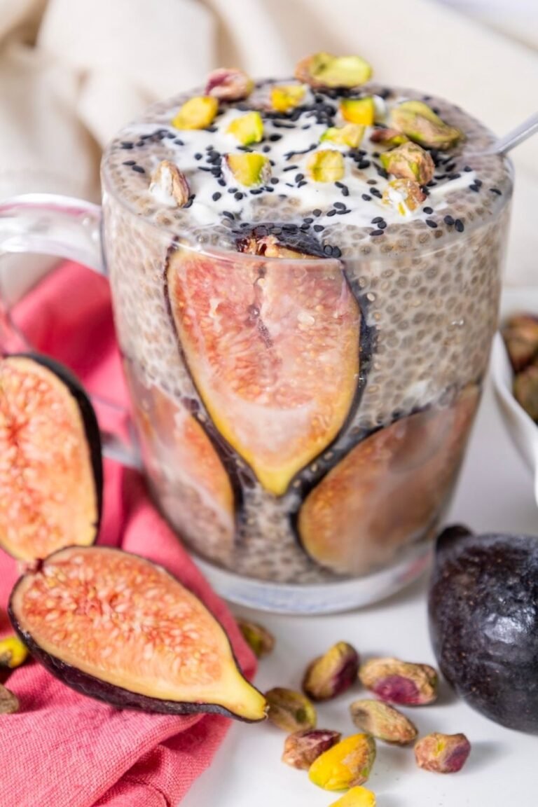 Glass jar filled with overnight chia pudding made with oat milk, layered with fresh fig slices and topped with pistachios and black sesame seeds.