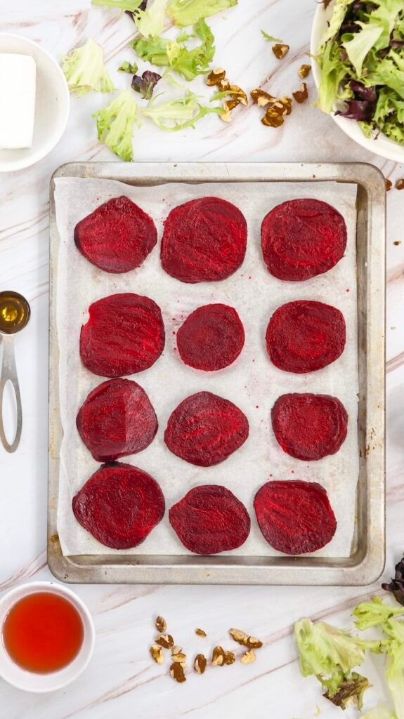 Thinly sliced beetroot roasting on a parchment-lined baking sheet, prepared.