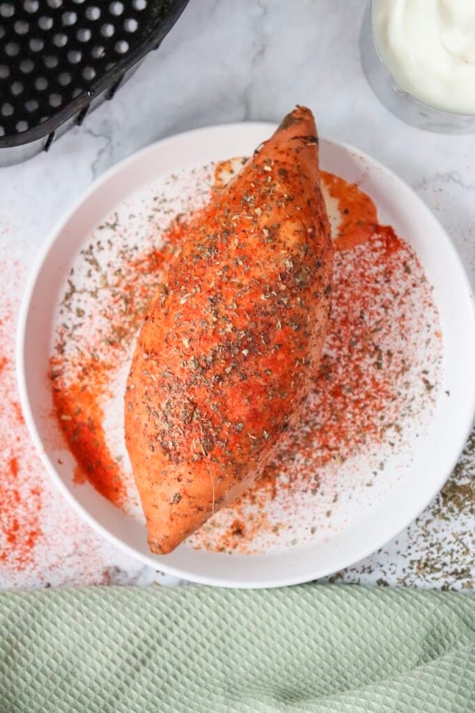 Whole sweet coated in paprika, dried basil, salt, and pepper on a white plate before cooking.