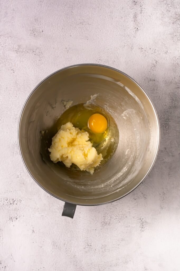 Egg added to creamed butter mixture in a stand mixer bowl.
