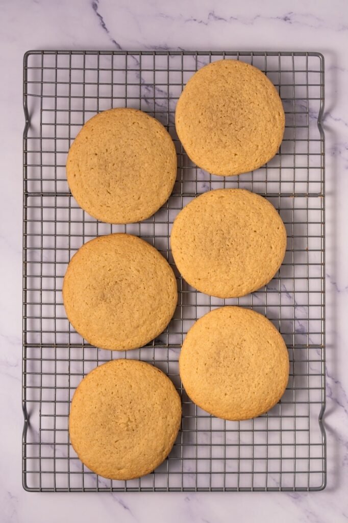 Freshly baked Crumbl cookie dough cookies cooling on a wire rack after baking, showing golden edges and soft centers.