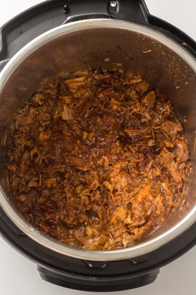 Tender shredded pork coated in BBQ sauce inside an Instant Pot after cooking, showing the finished Instant Pot pulled pork ready to serve.