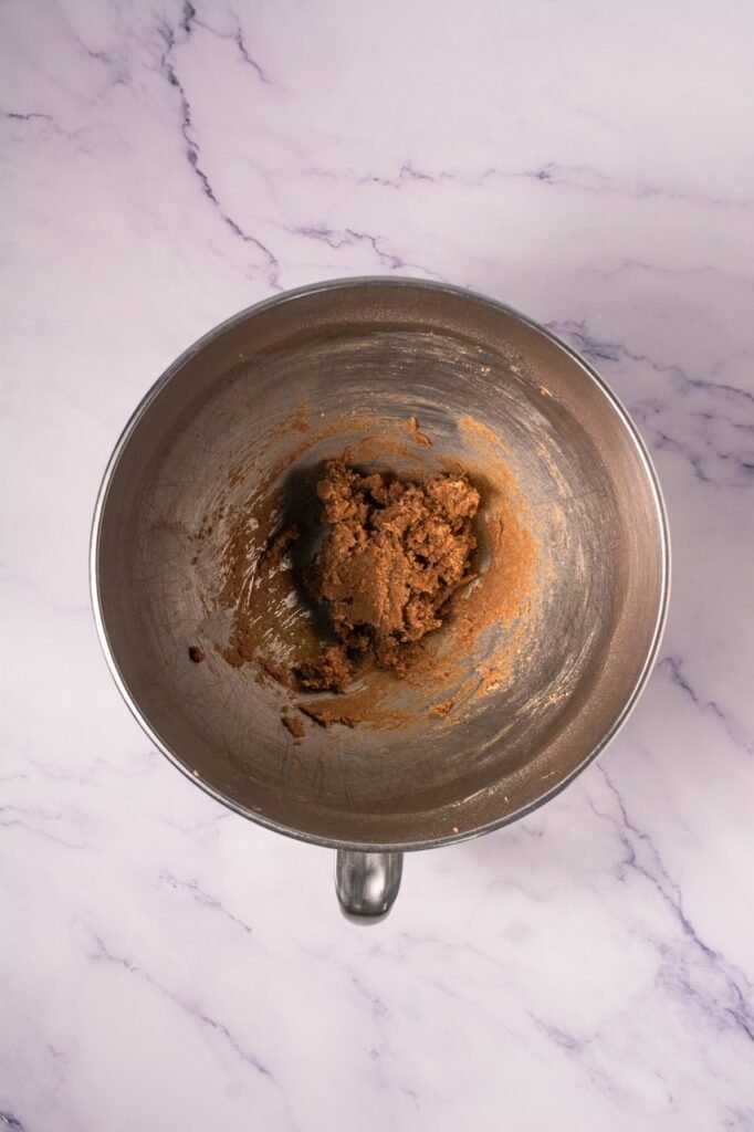 Overhead view of a metal mixing bowl on a marble countertop containing a cinnamon sugar and butter mixture being prepared for the topping used in Crumbl cinnamon swirl cookies.