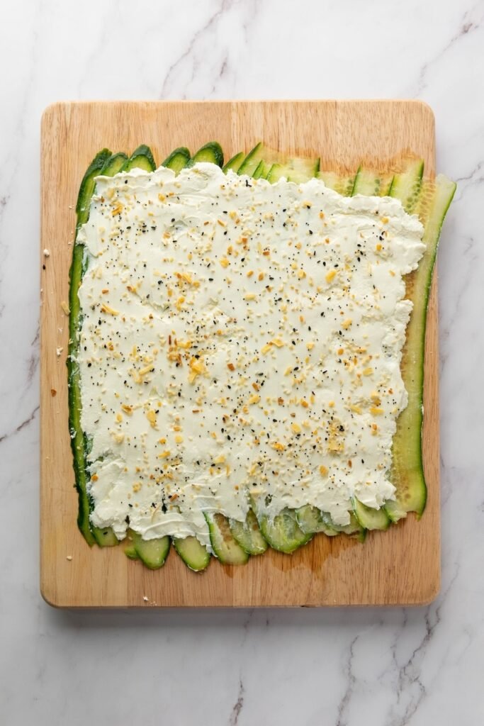 Cucumber ribbons layered on a cutting board and spread with cream cheese and everything bagel seasoning before adding smoked salmon.
