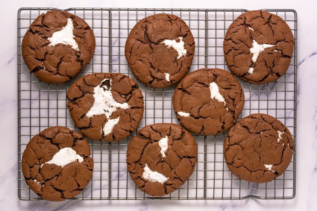 Freshly baked chocolate mallow cupcake cookies with marshmallow centers cooling on a metal rack after baking.
