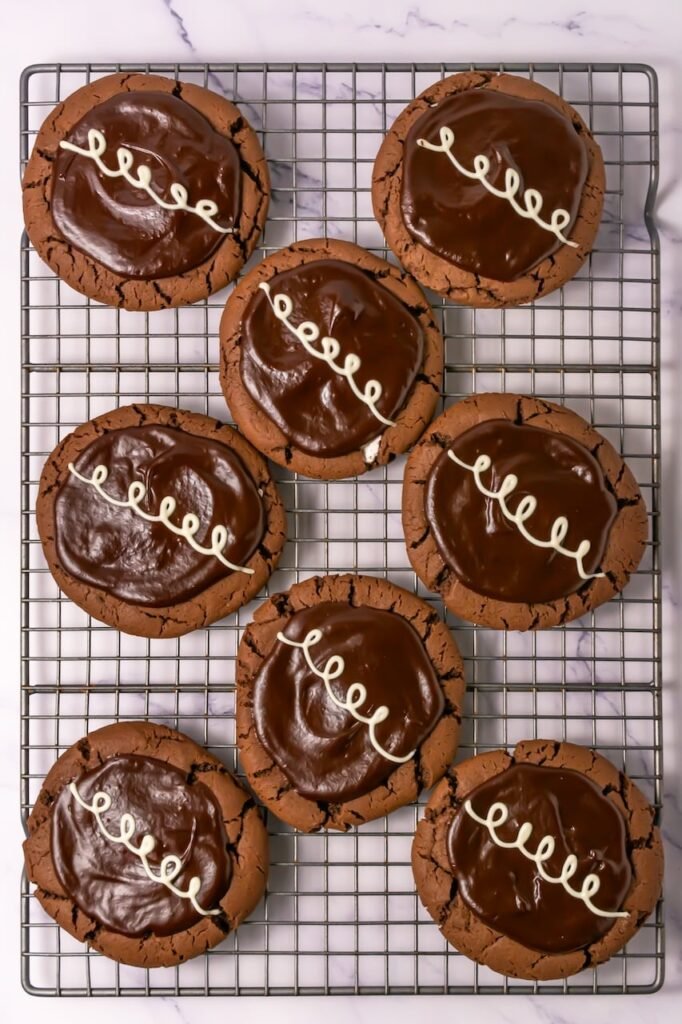 Finished Crumbl chocolate mallow cupcake cookies topped with chocolate ganache and white chocolate drizzle on a cooling rack.