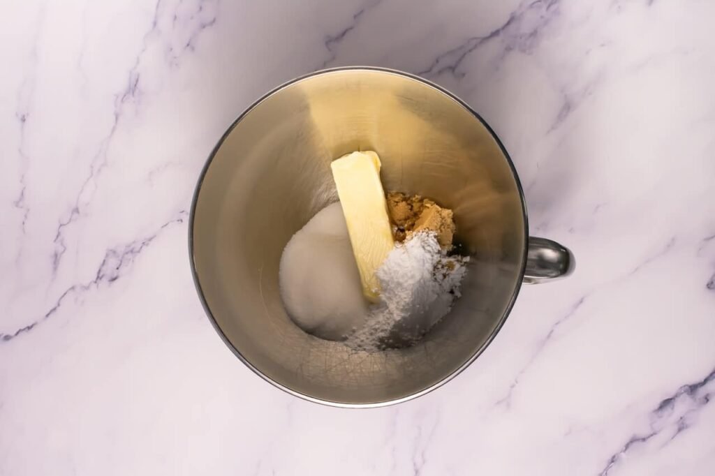 Overhead view of a mixing bowl with butter, granulated sugar, brown sugar, and powdered sugar before creaming for crumbl chocolate Oreo cookies.