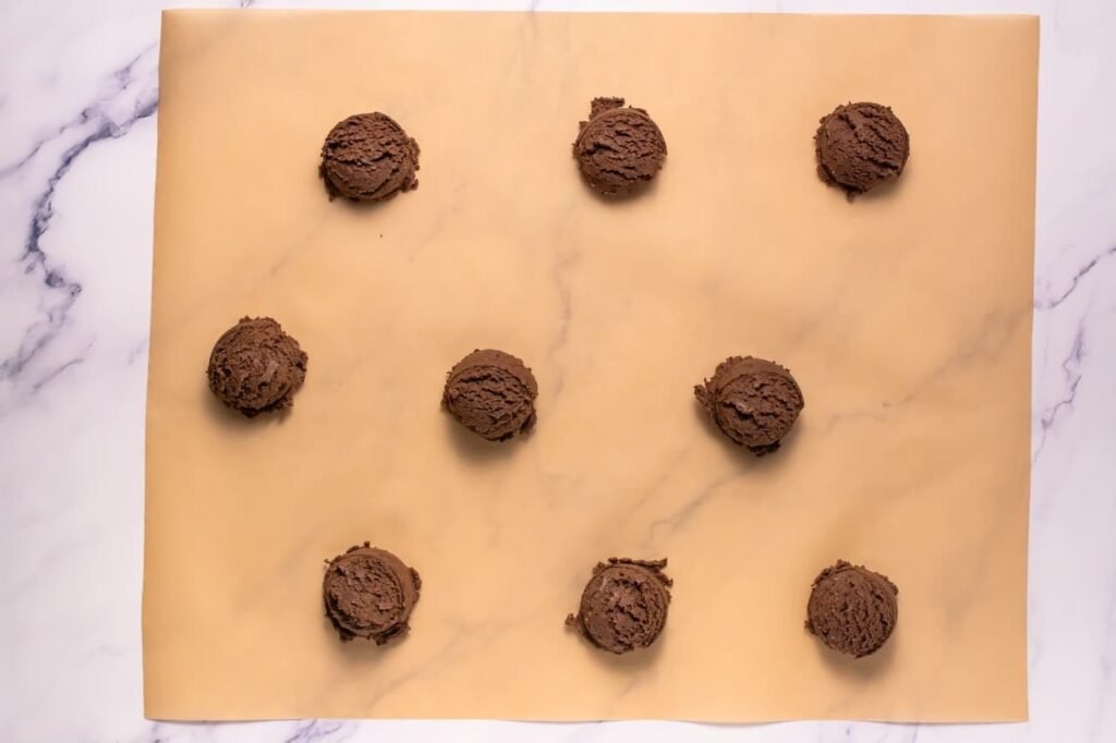 Overhead view of evenly scooped dough balls spaced on a parchment-lined baking sheet, ready to bake.