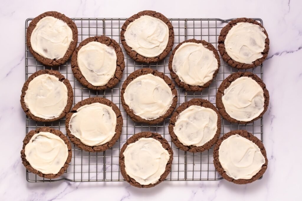 Overhead view of baked cookies spread with smooth frosting and arranged on a cooling rack, ready to serve.