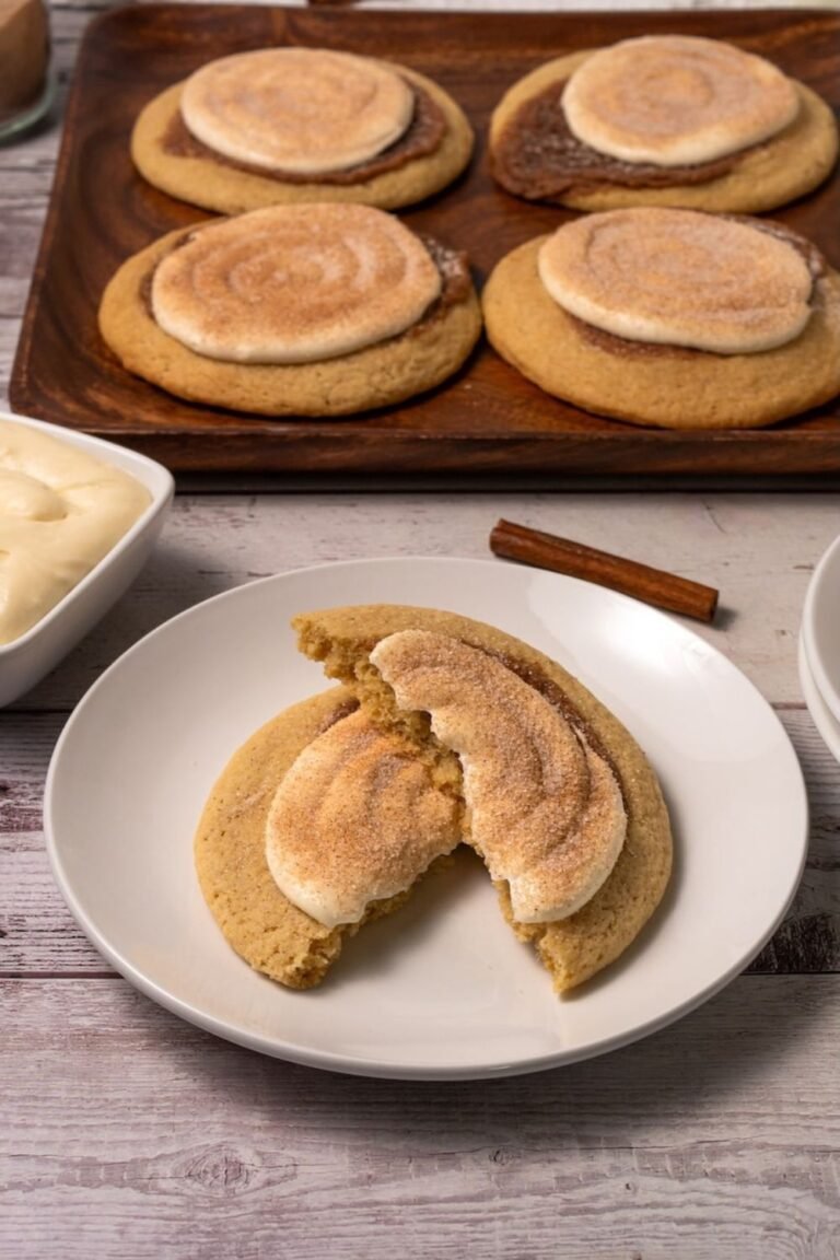 Overhead view of six baked Crumbl cinnamon swirl cookies on a wire cooling rack, each topped with cream cheese frosting and finished with a light cinnamon sugar sprinkle.