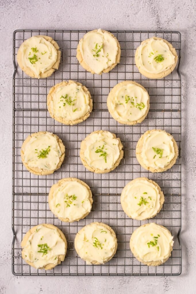 Overhead view of soft coconut lime cookies topped with lime buttercream frosting and fresh lime zest arranged on a wire cooling rack.