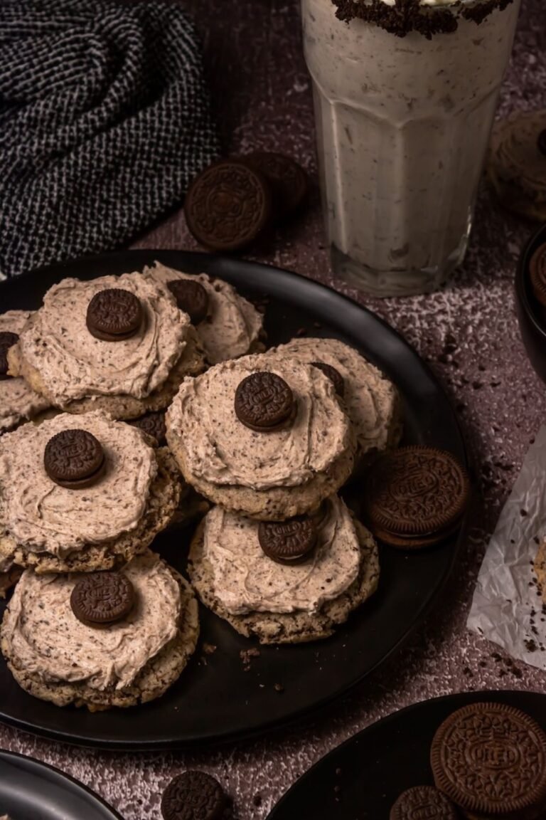 Plate of cookies and cream milkshake cookies topped with Oreo frosting and mini Oreos served beside a cookies and cream milkshake and Oreo cookies.