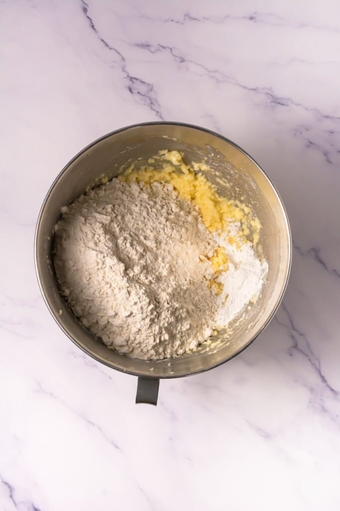 Stand mixer bowl with creamed butter mixture as flour and dry ingredients are added to make dough.