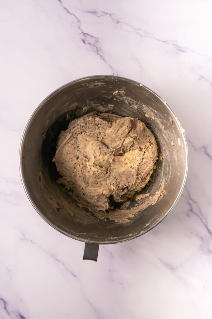 Stand mixer bowl filled with thick desserts and dough with crushed Oreo pieces mixed throughout.