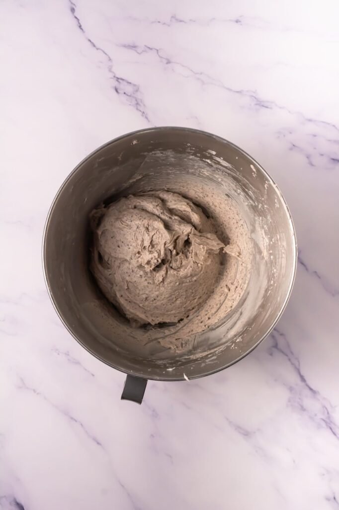 Overhead view of a stand mixer bowl filled with smooth frosting made with butter, powdered sugar, and crushed Oreos.