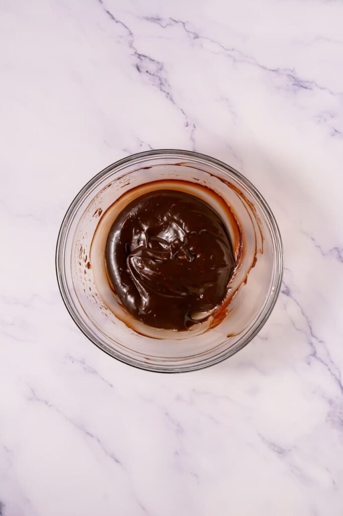 Small glass bowl of smooth chocolate ganache made with chocolate chips and cream for topping mallow cupcake cookies.