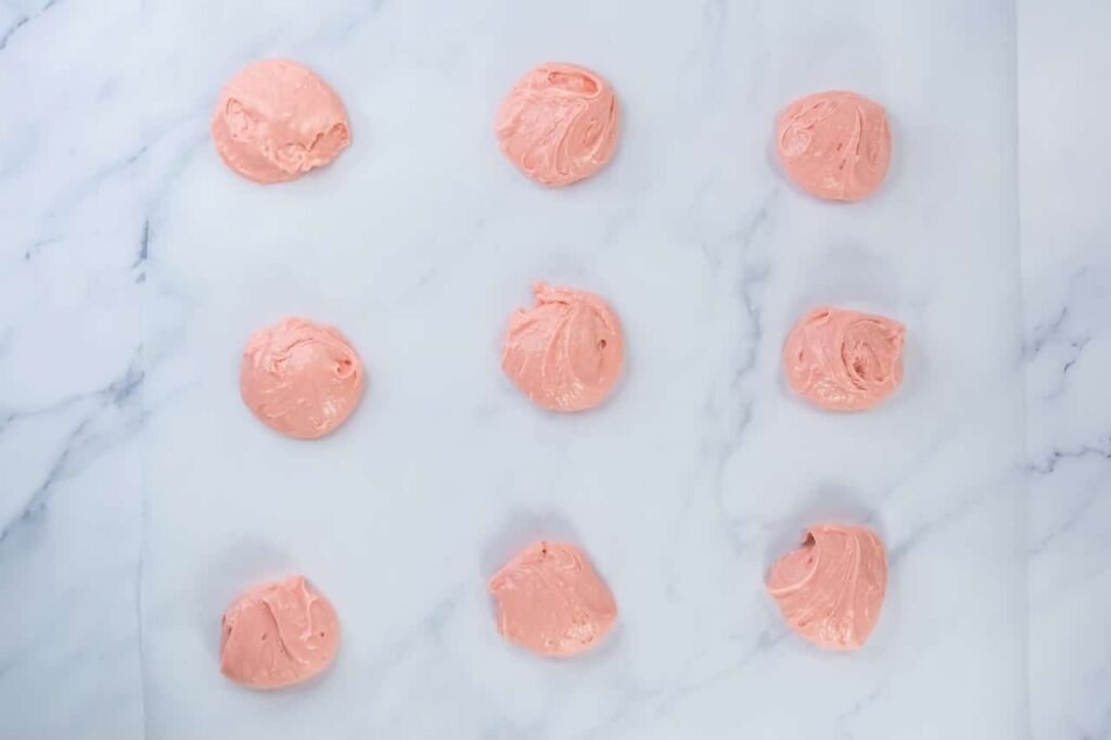 Evenly spaced scoops of strawberry cookie dough placed on parchment paper, ready to bake.