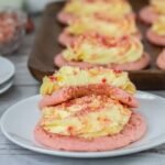 Close-up of strawberry shortcake cookies stacked on a plate, showing soft cookie layers with cream cheese frosting and crumb topping, highlighting texture and thickness.