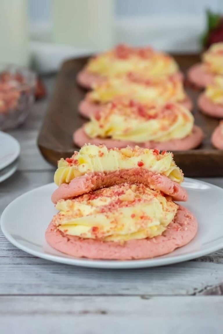Close-up of strawberry shortcake cookies stacked on a plate, showing soft cookie layers with cream cheese frosting and crumb topping, highlighting texture and thickness.