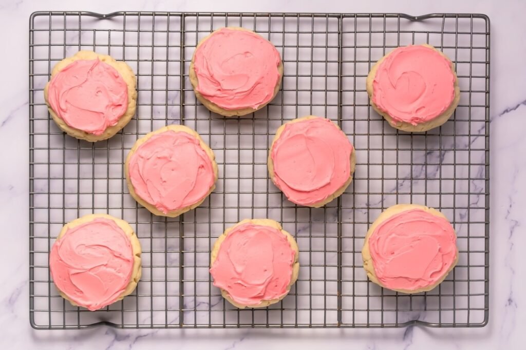 Overhead view of soft desserts topped with pink frosting arranged on a cooling rack, showing thick texture and smooth frosting swirls.