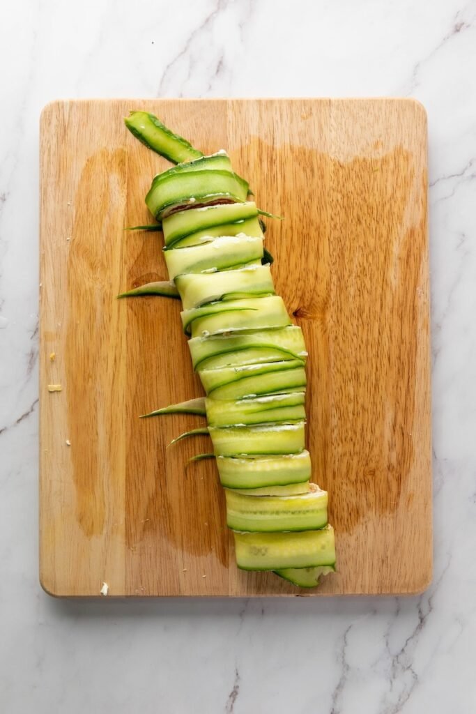 A rolled log made from thin ribbons wrapped around cream cheese and smoked fish sits on a wooden cutting board, partially sliced into bite-sized with the creamy filling visible between the layers.