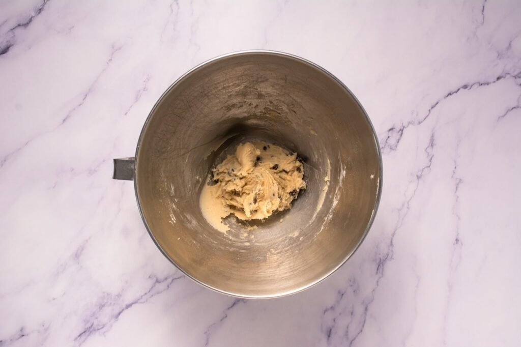 Edible dough with mini chocolate chips mixed in a stand mixer bowl for topping.