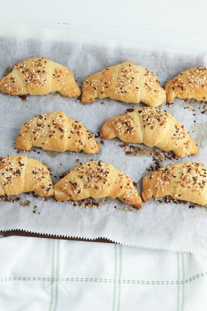 Freshly baked croissants topped with seasoning on a parchment-lined baking sheet.
