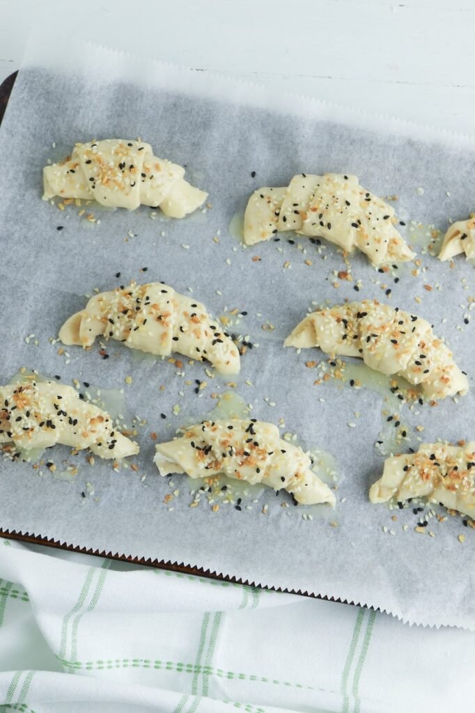 Unbaked crescent rolls topped with everything bagel seasoning on a parchment-lined baking sheet before baking.