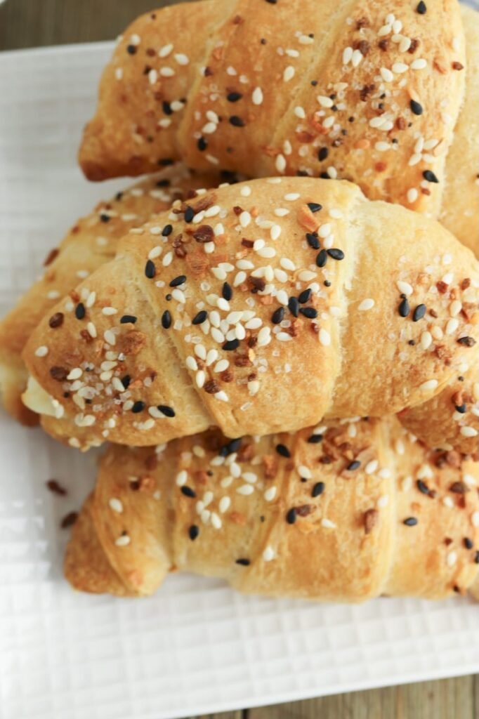 Close-up of flaky everything bagel crescent rolls baked golden brown and topped with sesame seeds, poppy seeds, garlic, and onion seasoning.