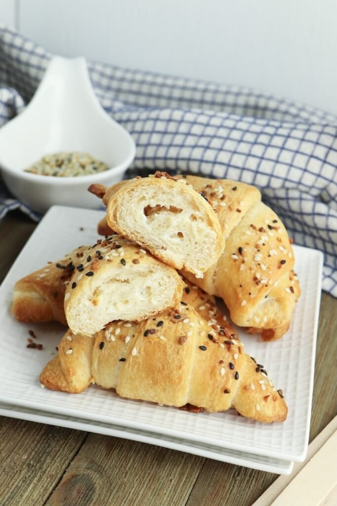 Flaky everything bagel crescent rolls cut open to show the soft layered interior and cream cheese filling, topped with sesame seeds, poppy seeds, garlic, and onion seasoning.