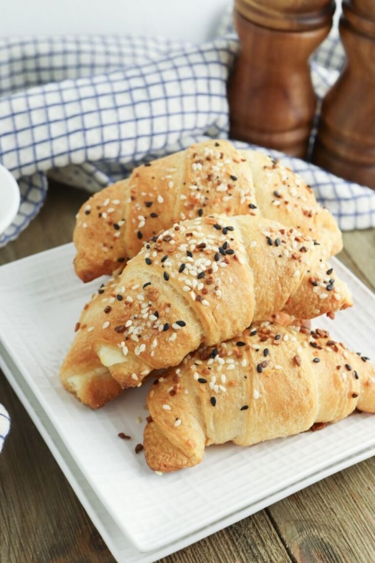Plate of flaky everything bagel crescent rolls topped with sesame seeds, poppy seeds, garlic, and onion seasoning.