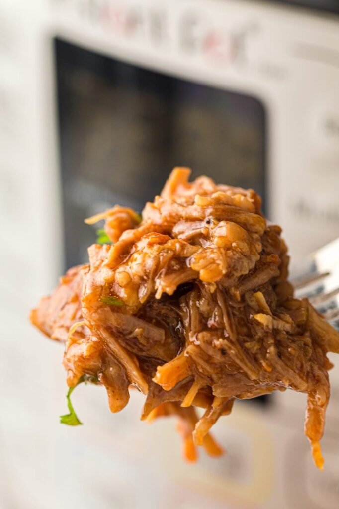 Close-up of tender shredded BBQ pulled pork on a fork, showing juicy texture from an Instant Pot pulled pork recipe.