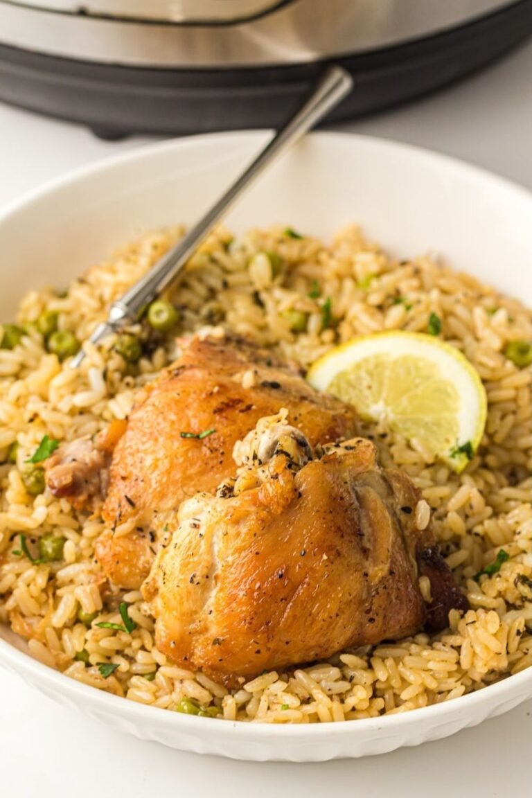 White bowl filled with Instant Pot chicken and rice topped with two golden-brown chicken thighs, fluffy seasoned rice, green peas, chopped herbs, and a lemon slice, with the Instant Pot visible in the background.