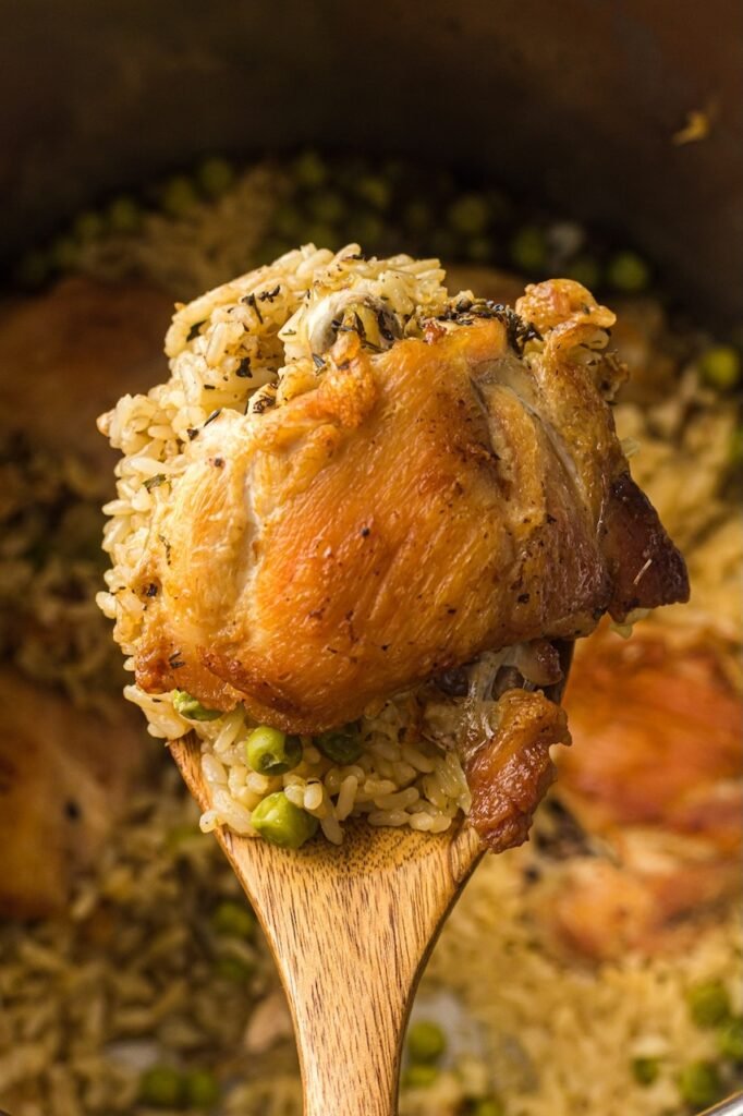 Spoonful of cooked Instant Pot chicken and rice with a browned chicken thigh, fluffy rice, and green peas lifted from the pressure cooker.