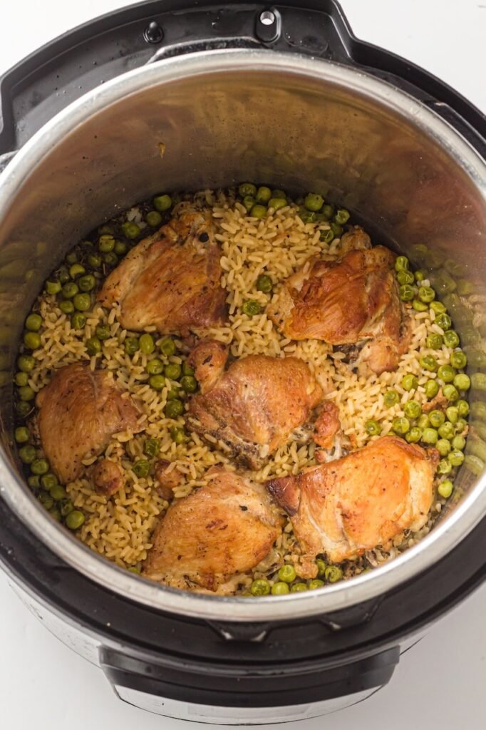 Cooked food with browned thighs, fluffy rice, and green peas inside the pressure cooker after cooking.